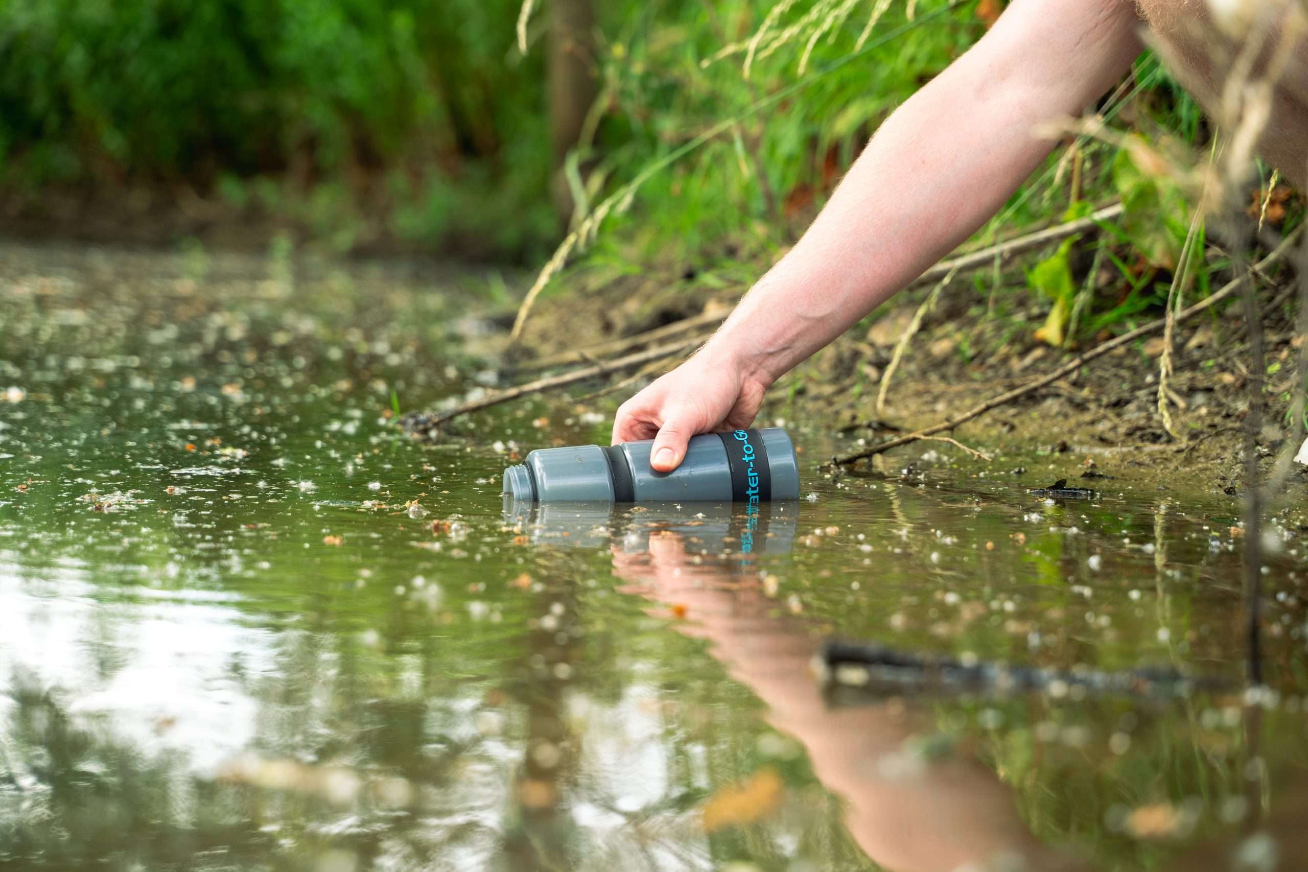 a water to go filter bottle being filled up in a very dirty and contaminated pond